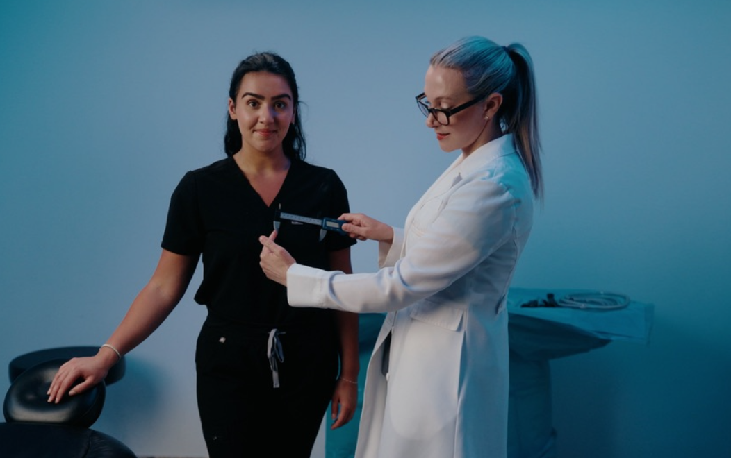 Dr. Beth Collins in a white medical coat using a digital caliper to take precise measurements for a patient in black scrubs, demonstrating the personalized care that makes her a top plastic surgeon in Connecticut.